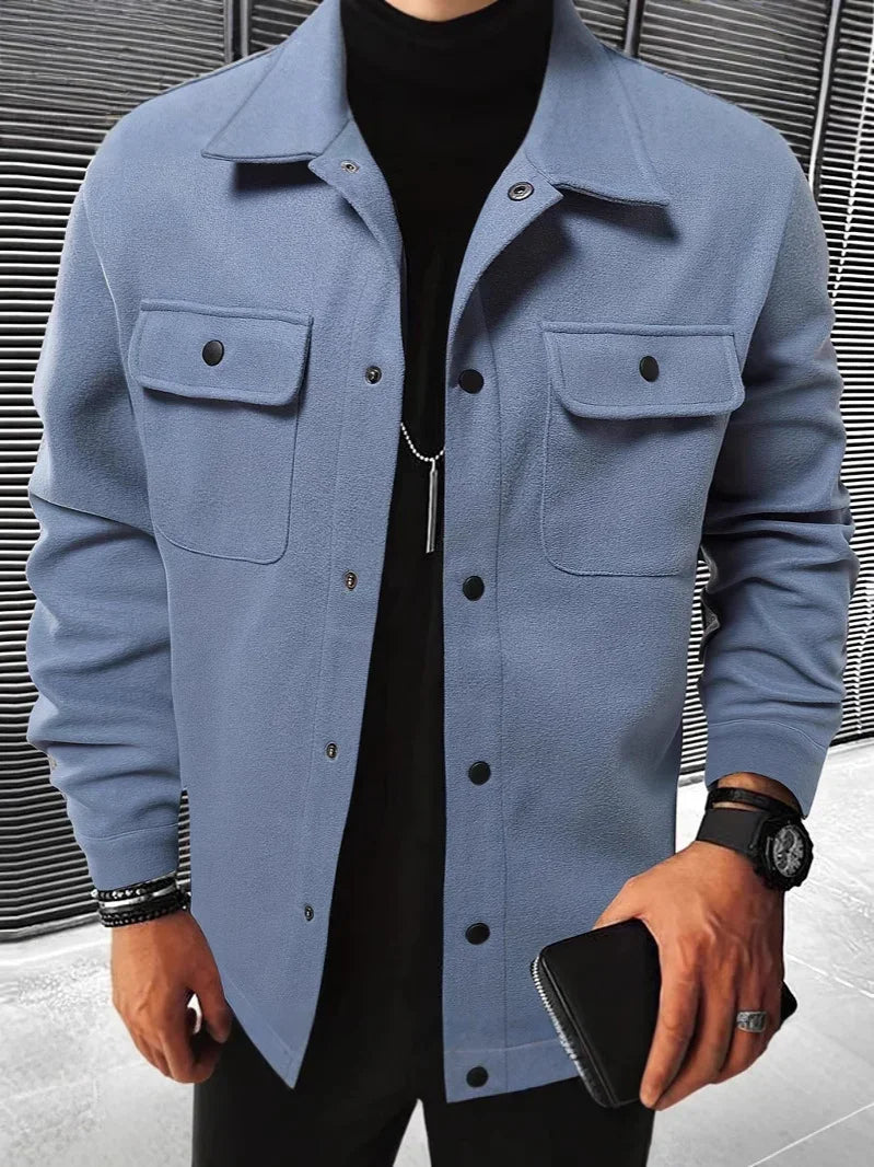 Man wearing light blue button-up jacket with breast pockets and black turtleneck, holding black wallet