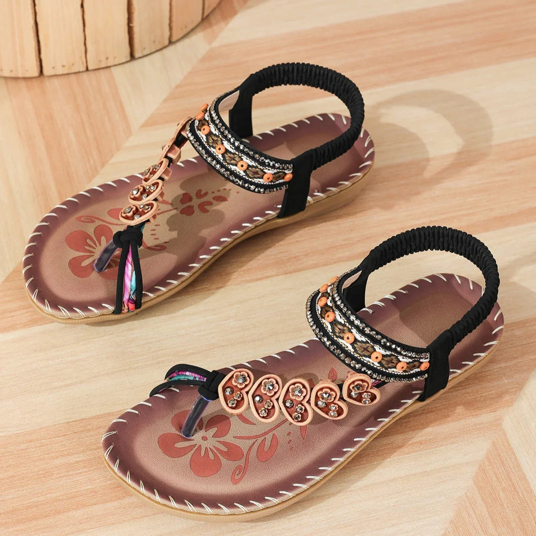 Pair of women's brown floral printed sandals with black elastic ankle straps and decorative beads