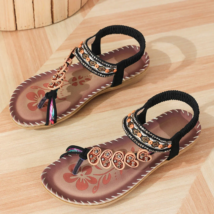 Pair of women's brown floral printed sandals with black elastic ankle straps and decorative beads