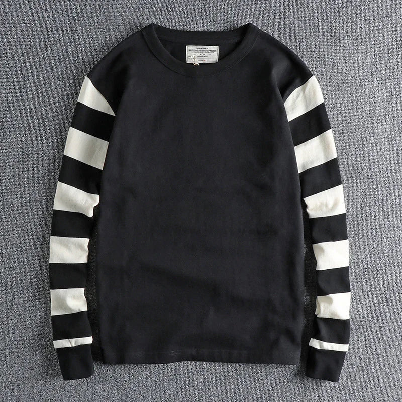 Black long-sleeve sweater with white horizontal stripes on sleeves, laid flat on grey surface