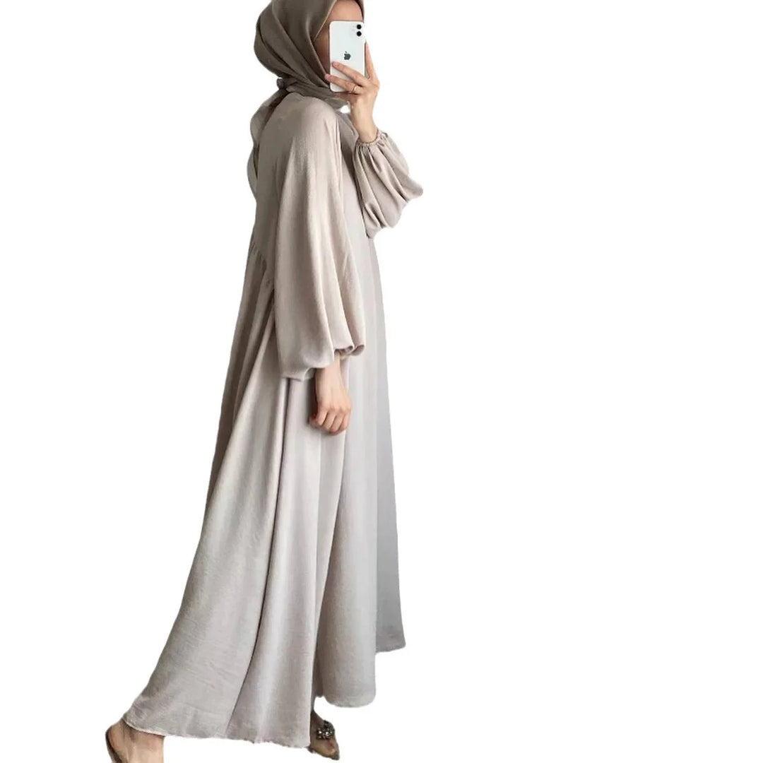 Woman wearing a loose beige abaya with balloon sleeves and khaki hijab, taking a mirror selfie