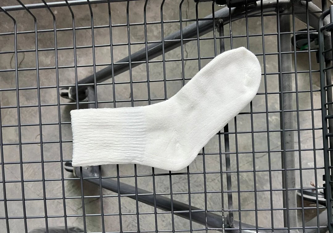 Single white cotton crew sock laid flat on a black wire mesh surface with concrete floor background
