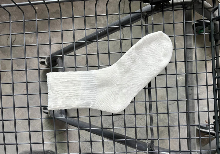 Single white cotton crew sock laid flat on a black wire mesh surface with concrete floor background