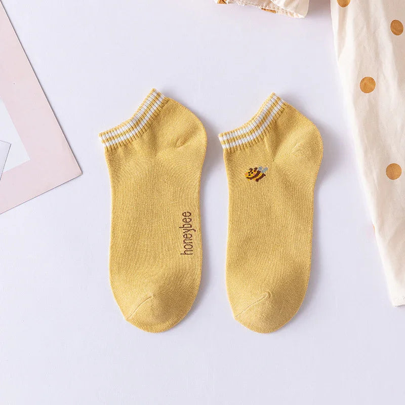 Pair of yellow ankle socks with white stripes and a small bee design on white background