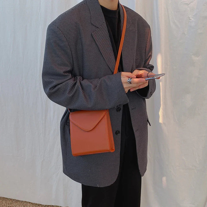 Person wearing checkered blazer and black outfit holding phone with brown crossbody bag