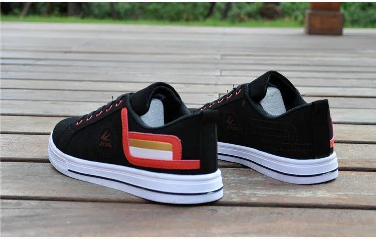 Pair of black casual sneakers with white soles and red-orange accents on wooden deck outdoors