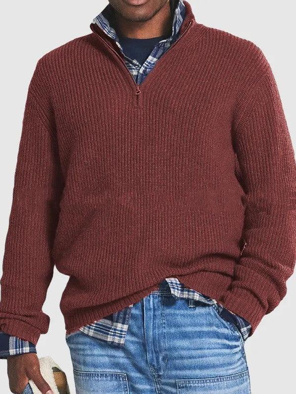 Man wearing maroon knit quarter-zip sweater over blue plaid shirt with blue jeans holding a book