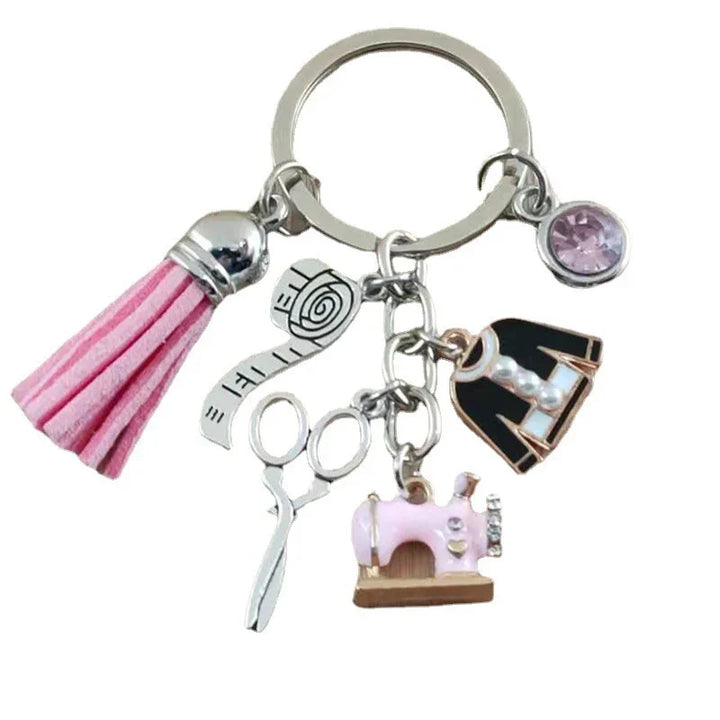 Sewing-themed keychain with pink tassel, silver scissors, measuring tape, pink sewing machine, black dress charm, and pink gem