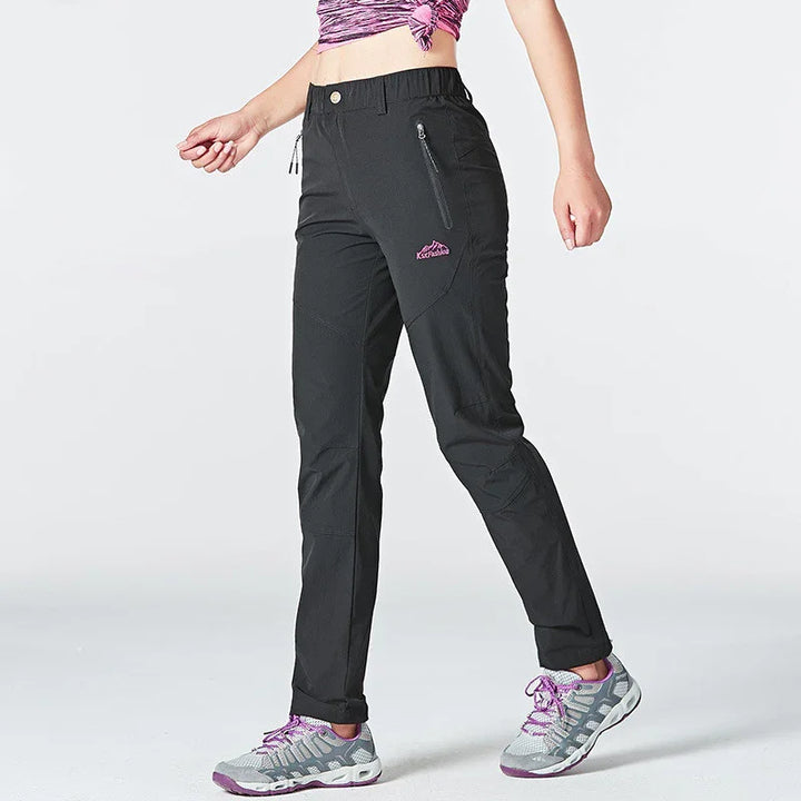 Woman wearing black outdoor hiking pants with zippered pocket and gray purple sneakers