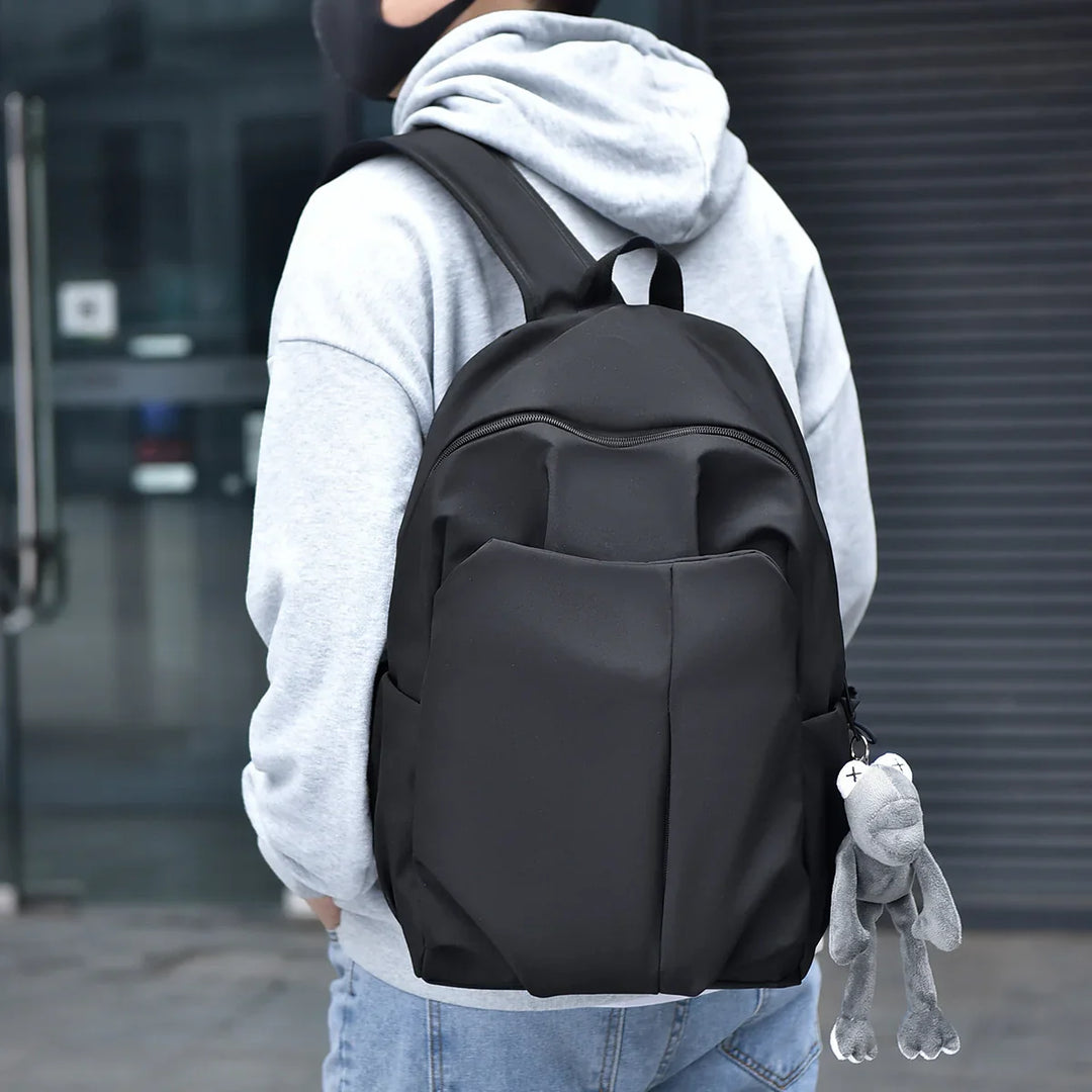 Person wearing grey hoodie and blue jeans with black backpack and grey plush keychain in urban setting