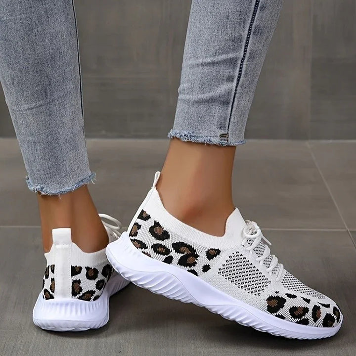White knit sneakers with black and brown leopard print worn with light blue frayed jeans on tile floor