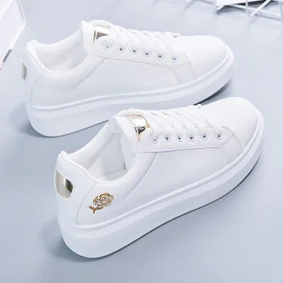 White platform sneakers with gold rose embroidery on heel and gold accent on tongue against gray background