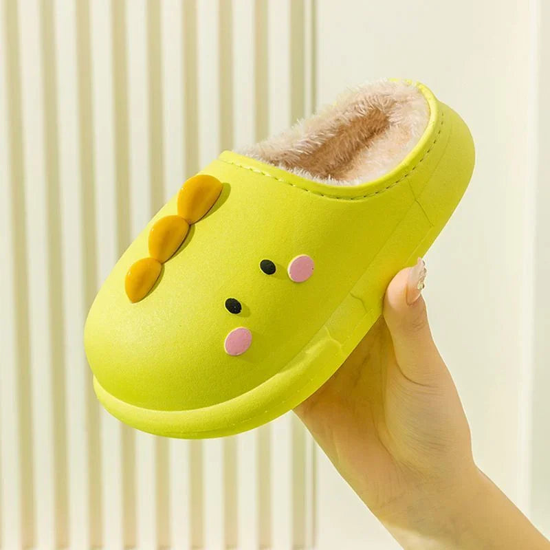 Hand holding bright yellow cute kids' indoor slippers with cartoon face and soft fur lining