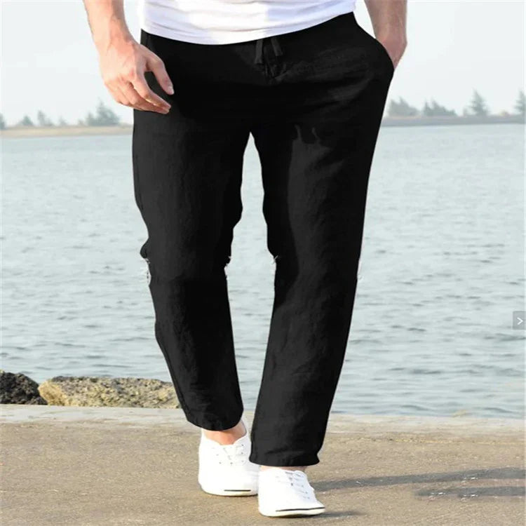 Man wearing black casual pants and white sneakers walking by the waterfront on a sunny day