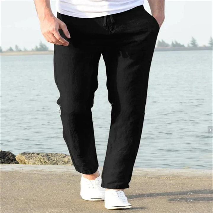 Man wearing black casual pants and white sneakers walking by the waterfront on a sunny day