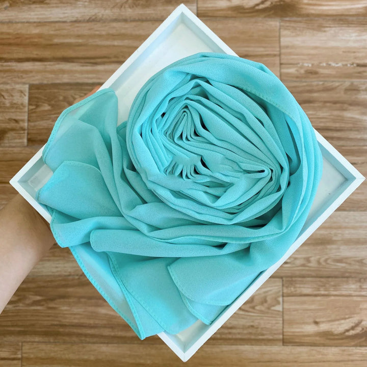 Hand holding a white tray with a neatly rolled turquoise fabric on wood floor background