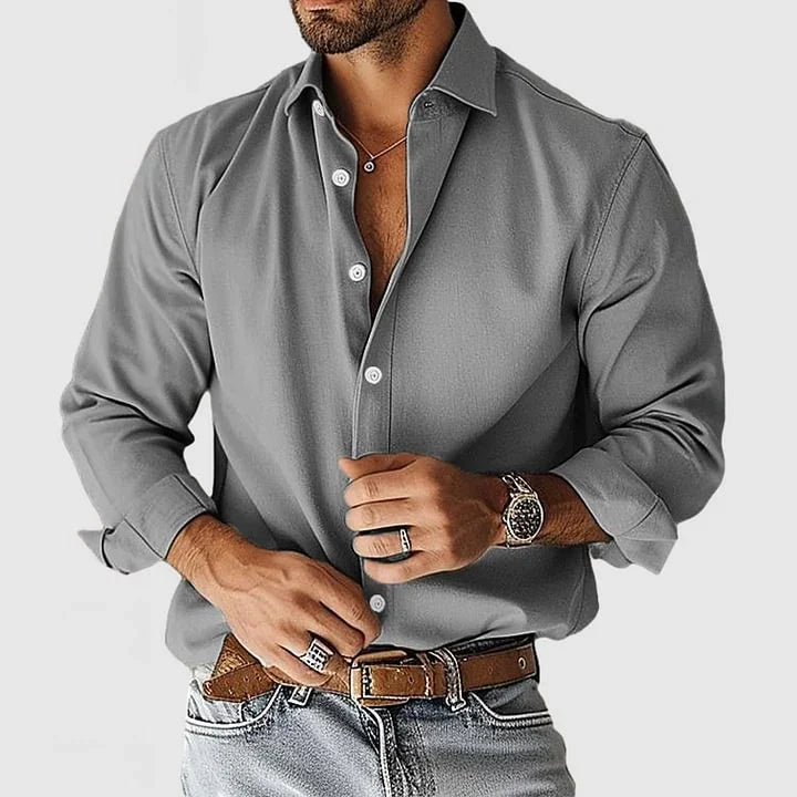 Man wearing gray long-sleeve button-up shirt, brown belt, light denim jeans, wristwatch, and rings