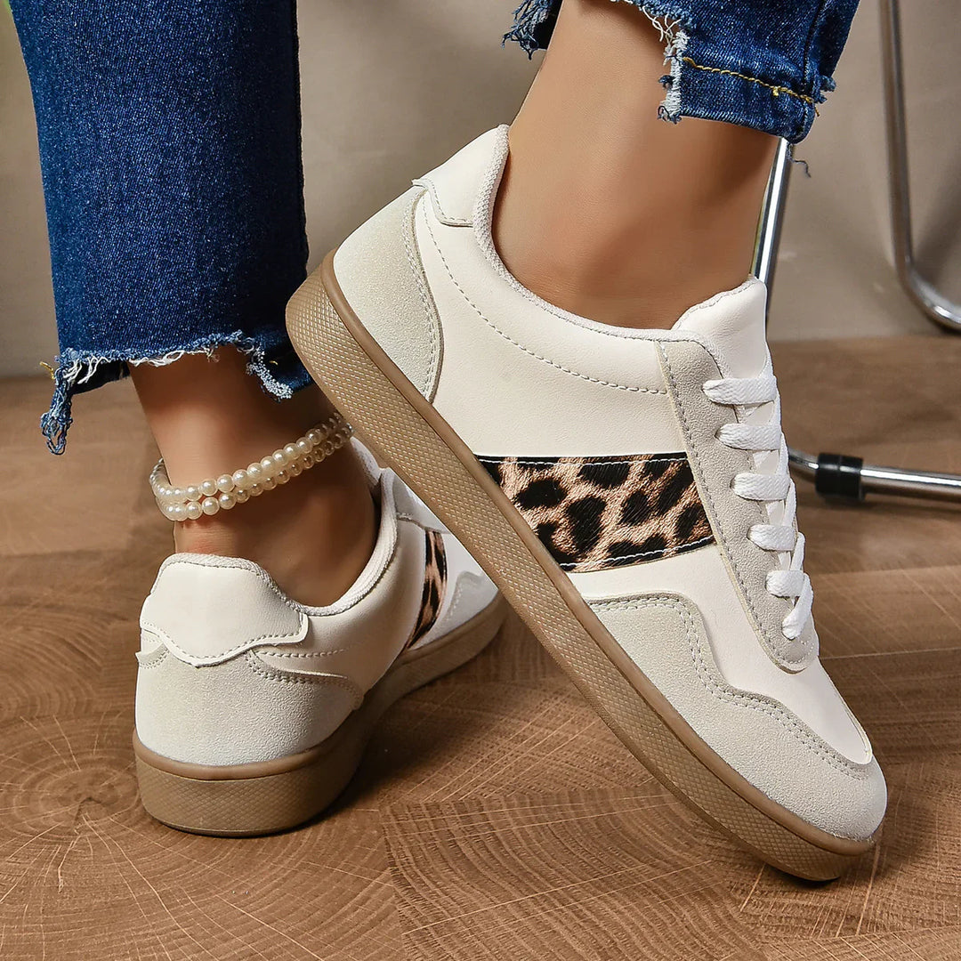 White casual sneakers with leopard print detail worn with frayed blue jeans and pearl anklet on wooden floor