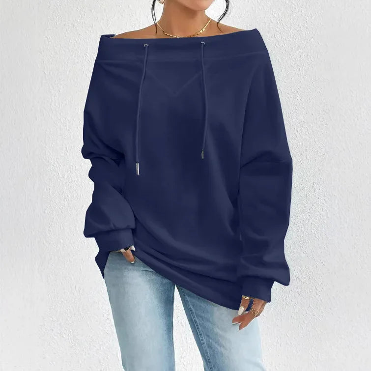 Woman wearing a navy off-shoulder hoodie and light blue jeans against white textured wall