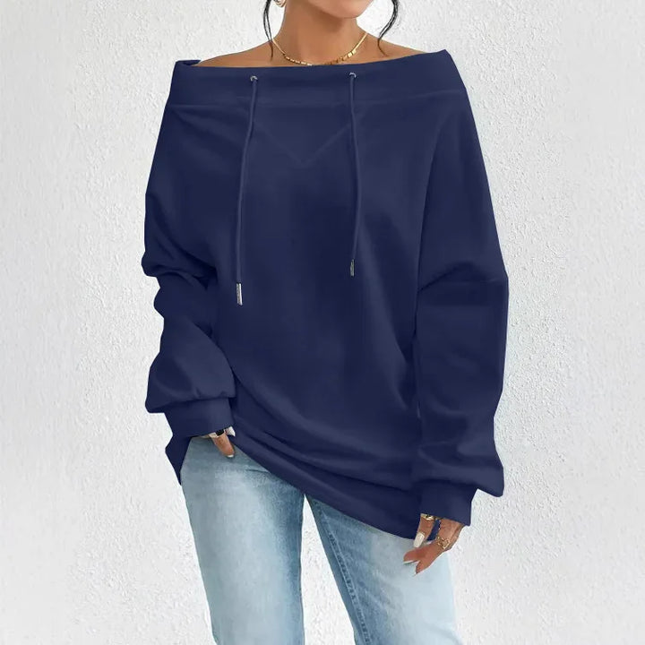 Woman wearing a navy off-shoulder hoodie and light blue jeans against white textured wall