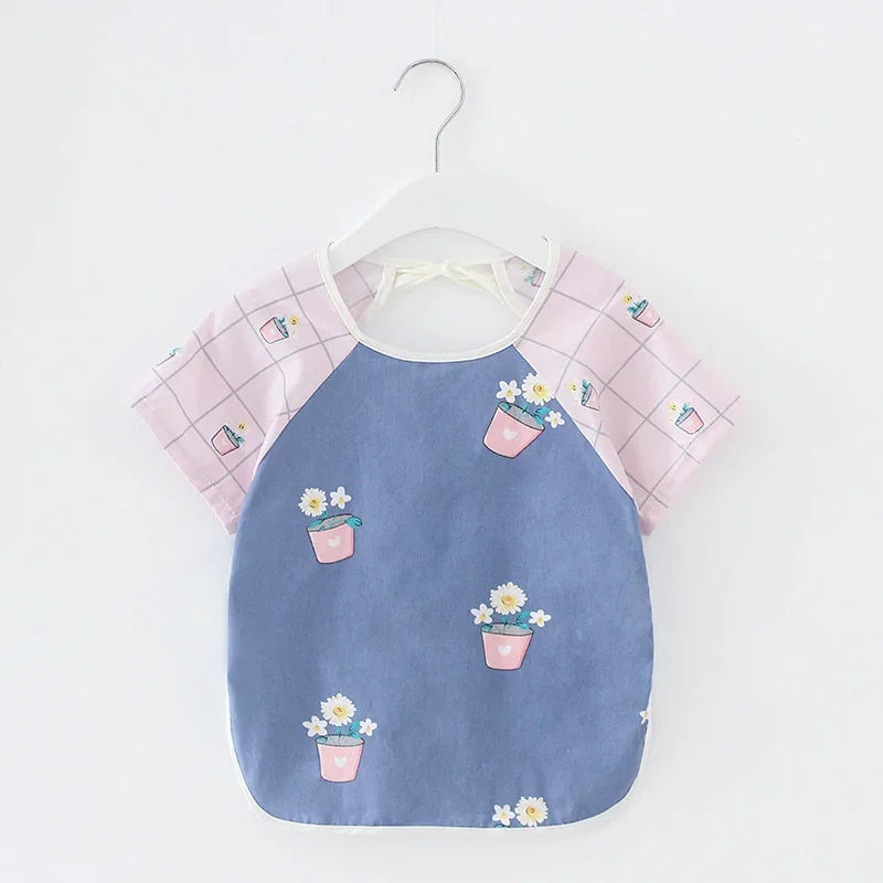 Baby bib with pink checkered sleeves and floral pot print on blue front, hanging on white hanger