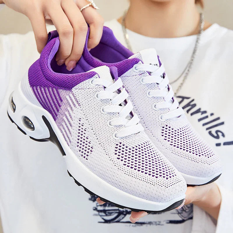 Lightweight purple and white mesh running shoes with cushioned soles held by a person in casual clothing