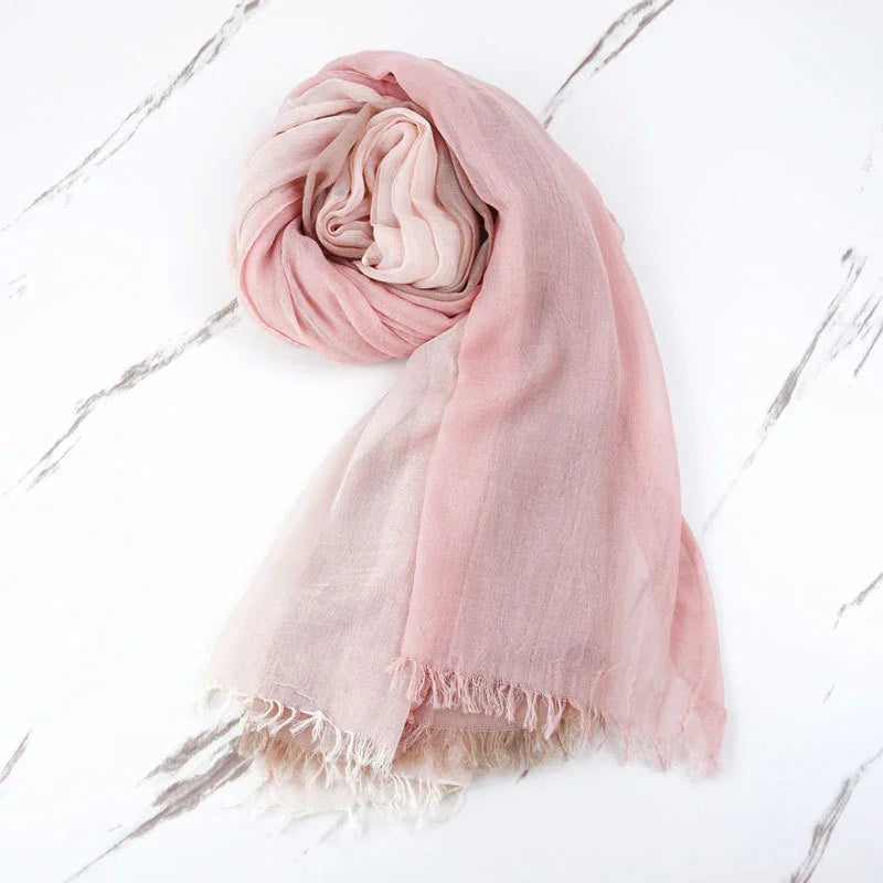Soft pink gradient scarf rolled on white marble surface with fringed edges
