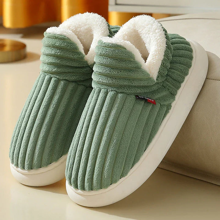 Green corduroy cozy slippers with white plush lining and white soles on beige surface