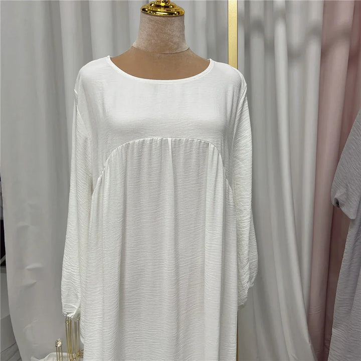 White long sleeve textured loose dress on a mannequin with gold neck detail in a fabric backdrop