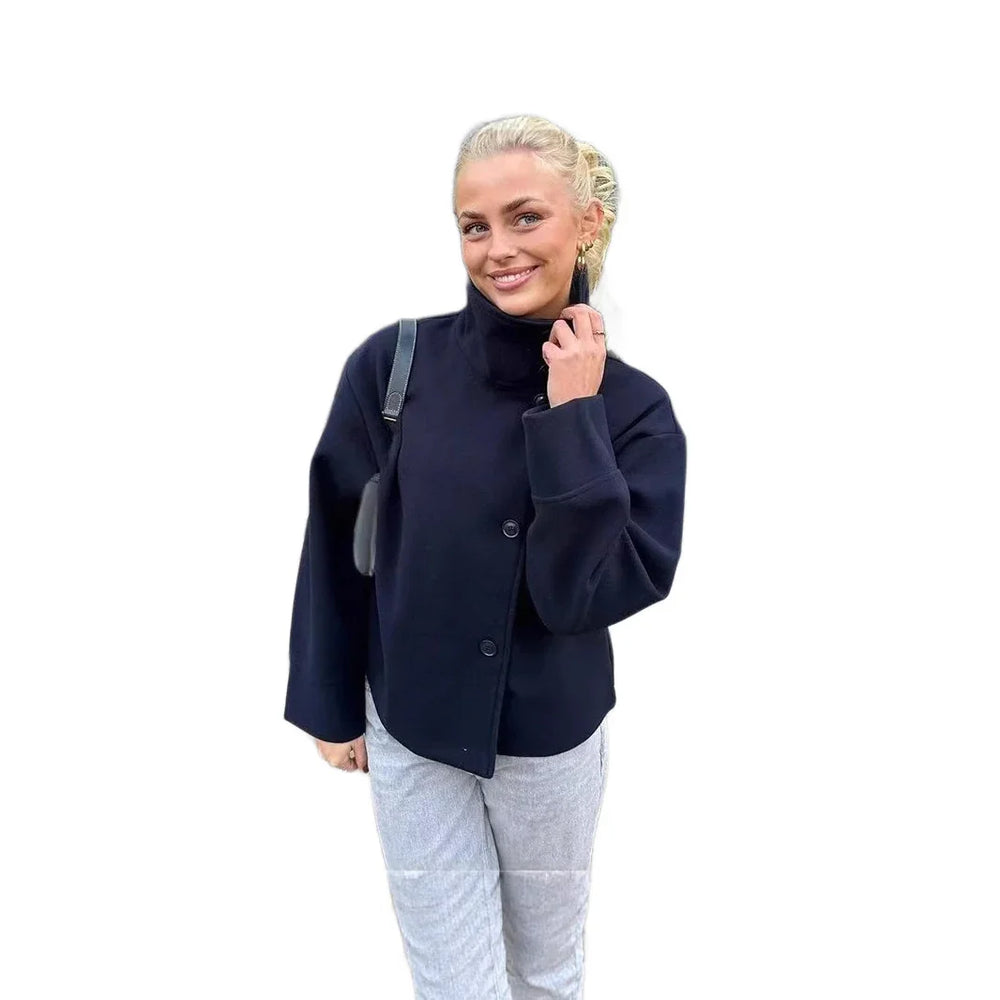 Smiling woman wearing black buttoned jacket and light gray pants with black shoulder bag