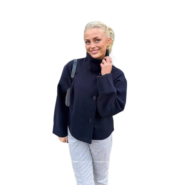 Smiling woman wearing black buttoned jacket and light gray pants with black shoulder bag