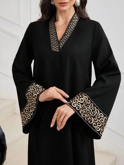 Black abaya with gold embroidered V-neck and wide cuffs, worn by woman with gold earrings and rings