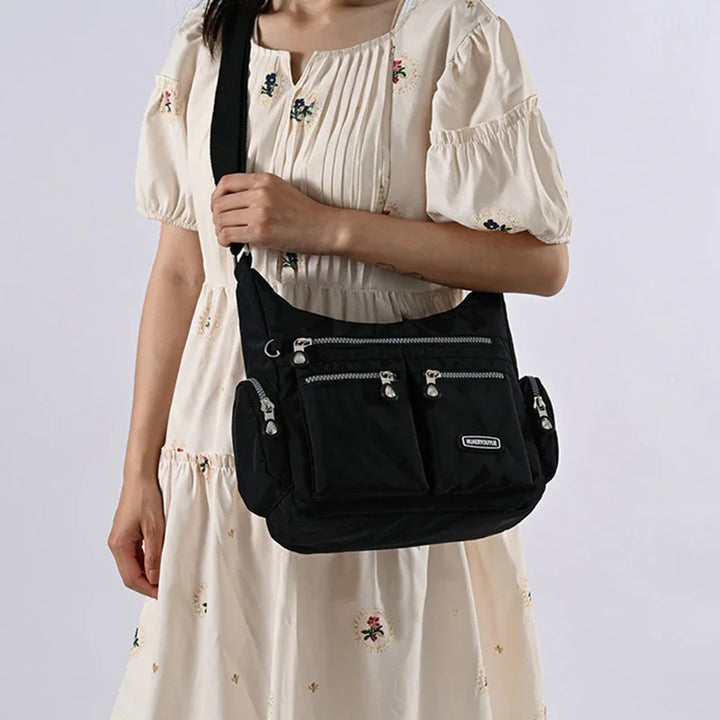 Woman wearing a cream floral dress holding a black multi-pocket crossbody bag