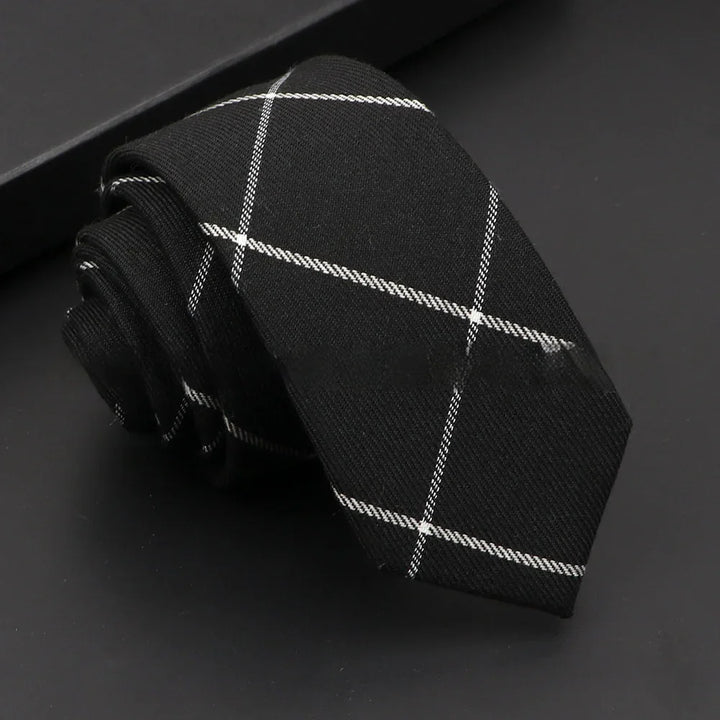 Black necktie with white plaid pattern folded on black surface