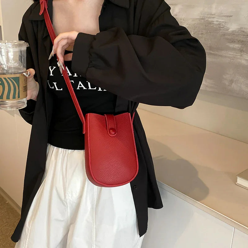 Woman wearing black jacket and white pants with red leather crossbody bag holding Starbucks cup