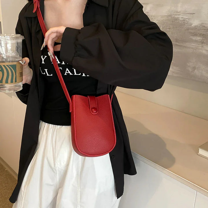Woman wearing black jacket and white pants with red leather crossbody bag holding Starbucks cup