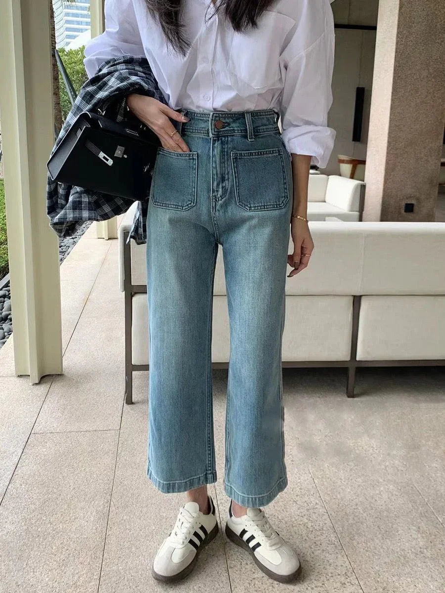 Woman wearing light blue wide-leg jeans, white shirt, white sneakers, holding black bag and plaid jacket