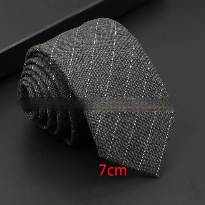 Gray pinstripe necktie rolled on black surface with 7cm width label