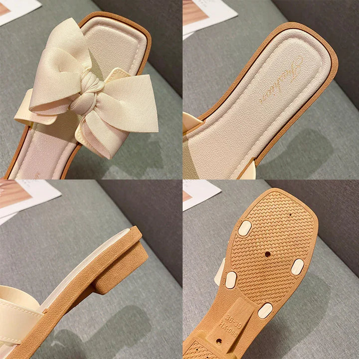 Cream-colored flat slide sandal with large fabric bow, square toe, and textured tan sole