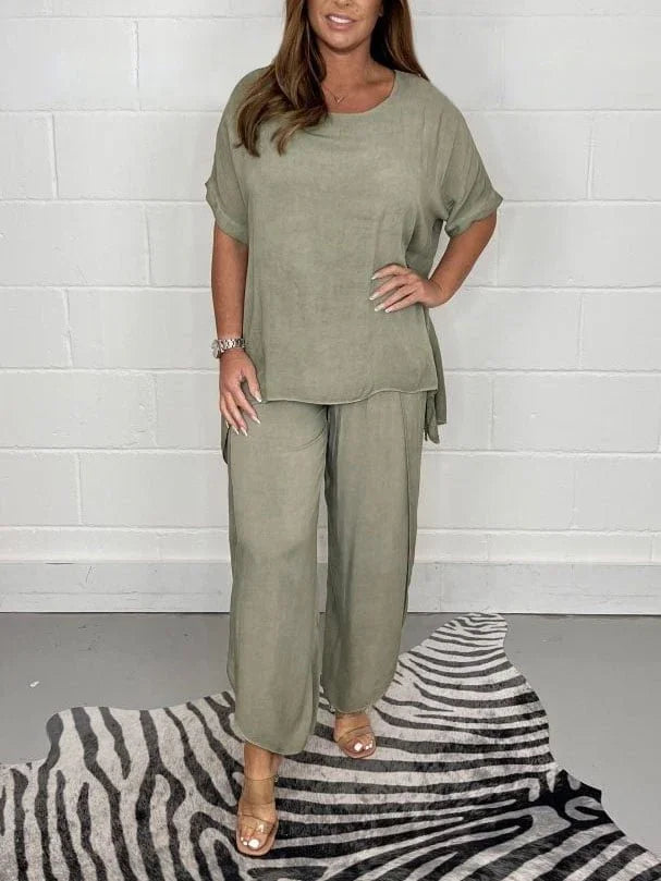 Woman wearing olive green loose top and wide-leg pants standing on zebra print rug against white brick wall
