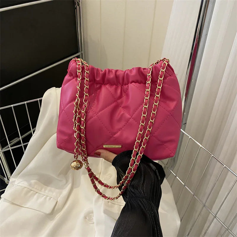 Pink quilted handbag with gold chain strap and decorative charm held over white garment and wire basket