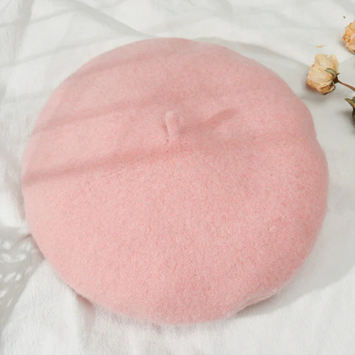 Soft pink wool beret on a white fabric background with dried flowers nearby