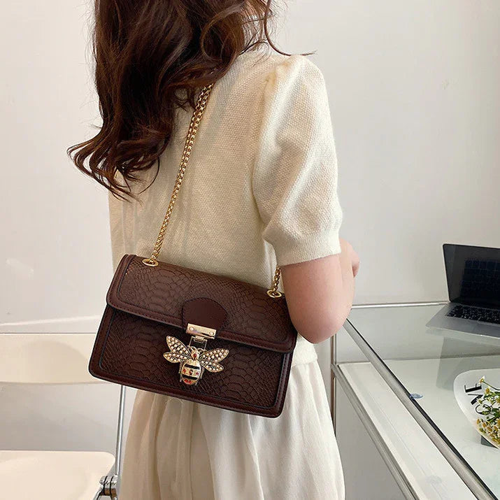 Woman wearing cream dress with textured short sleeves carrying brown leather handbag with gold bee decoration
