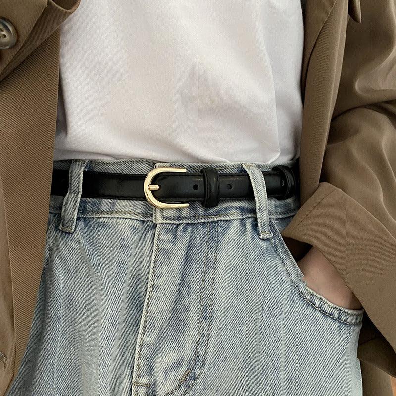 Close-up of casual outfit with black leather belt, light blue jeans, white top, and brown blazer sleeve