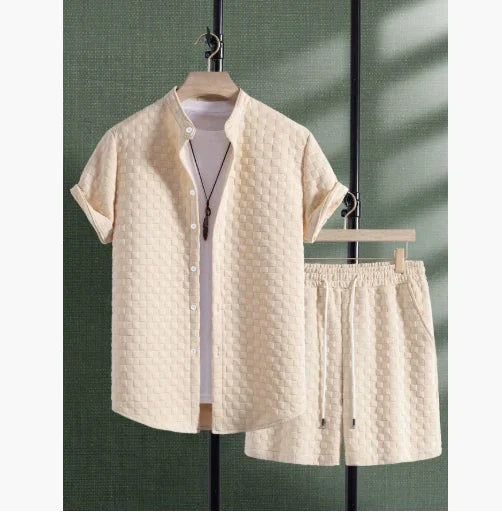 Beige textured short-sleeve button-up shirt and matching shorts hung on black rack against green wall