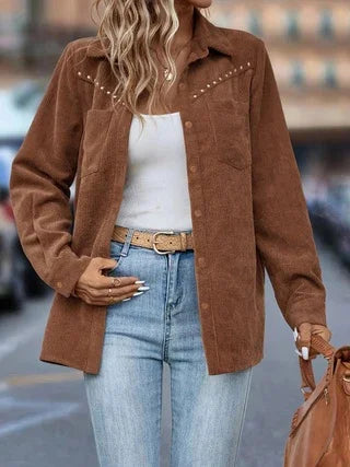 Woman wearing brown studded button-up corduroy shirt jacket with white top and blue jeans