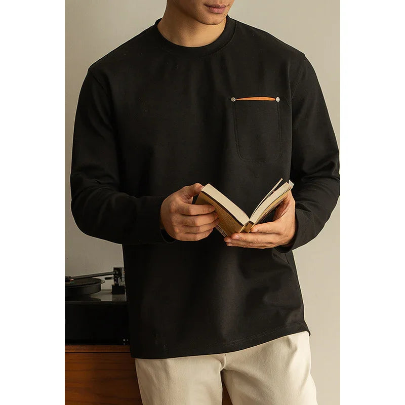 Man wearing black long-sleeve shirt with chest pocket holding an open book indoors