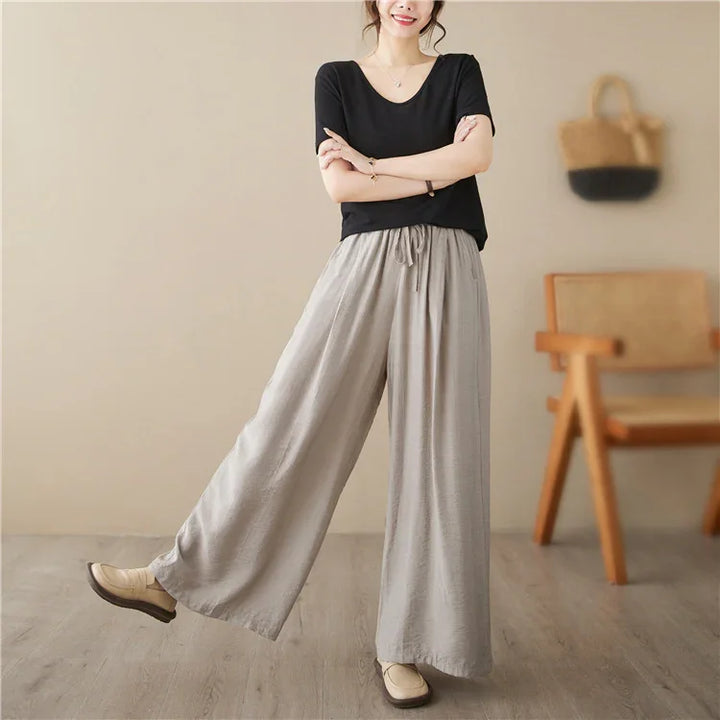 Woman wearing black short-sleeve top and loose wide-leg light gray pants in neutral minimalist room