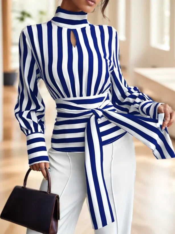 Woman wearing blue and white vertical striped blouse with tie waist and white pants, holding black handbag