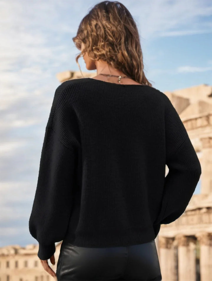 Woman with wavy hair wearing a black sweater and leather pants outdoors against an ancient stone building